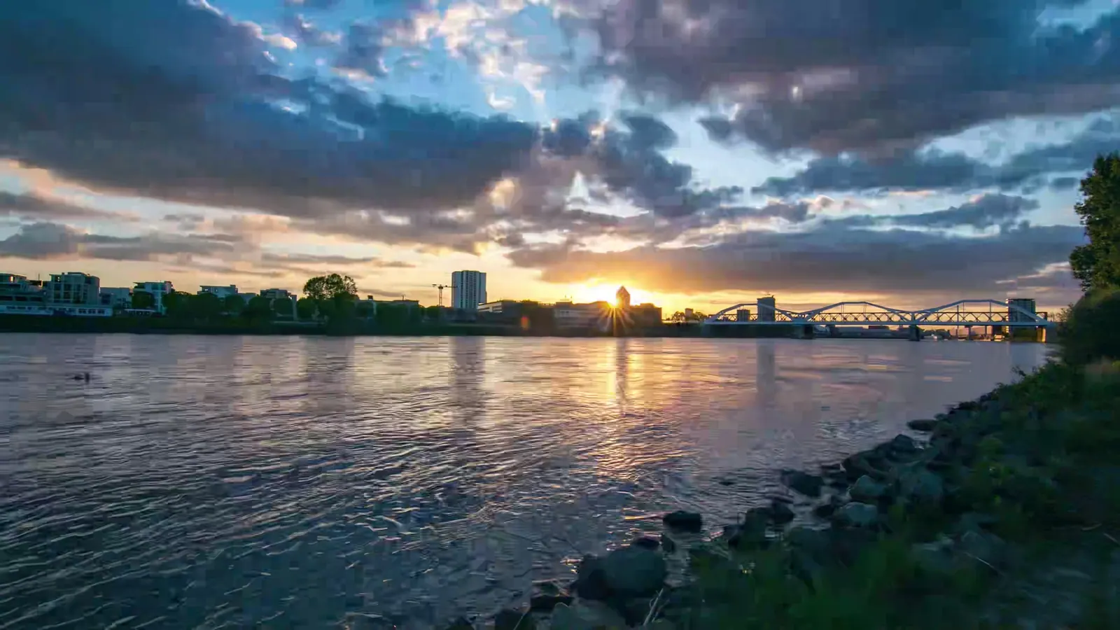 Rheinufer in Ludwigshafen bei Sonnenuntergang mit Stadtsilhouette und Brücke