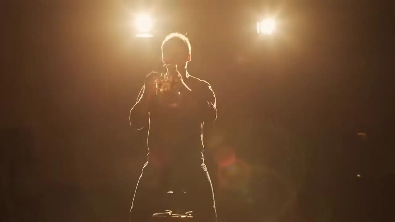 Filmstill: Musiker mit Blasinstrument im warmen Gegenlicht einer Bühne