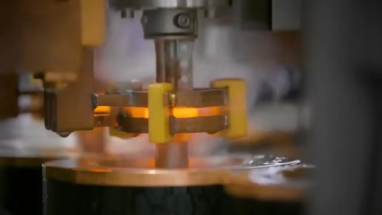 Filmstill: glühendes Werkstück zwischen Greifern einer Industriemaschine