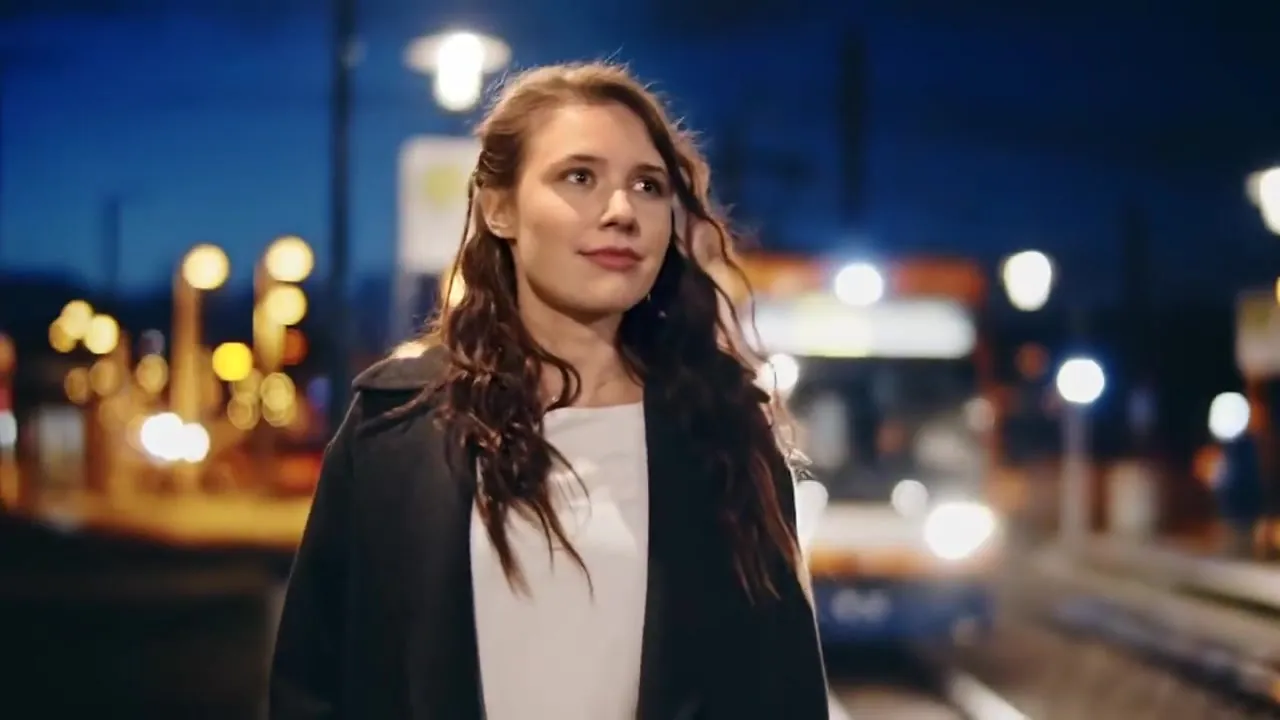 Filmstill: junge Frau an einer Straßenbahnhaltestelle bei Nacht