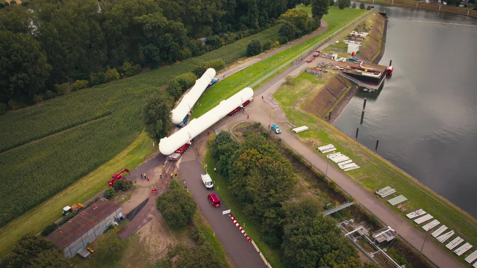 Luftbild eines Schwertransports mit einem weißen Tank auf einer Straße am Flussufer