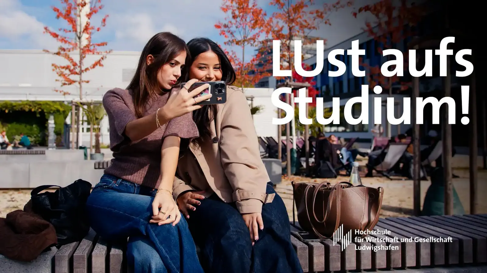 2 Studentinnen machen auf dem Campus ein Selfie, Schriftzug „LUst aufs Studium!“