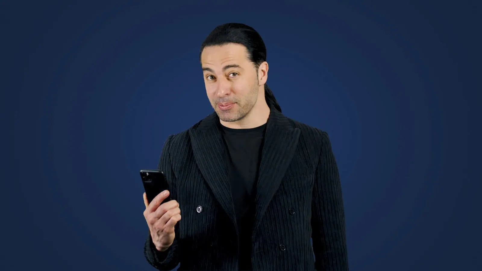 Bülent Ceylan mit Smartphone in der Hand vor dunkelblauem Hintergrund