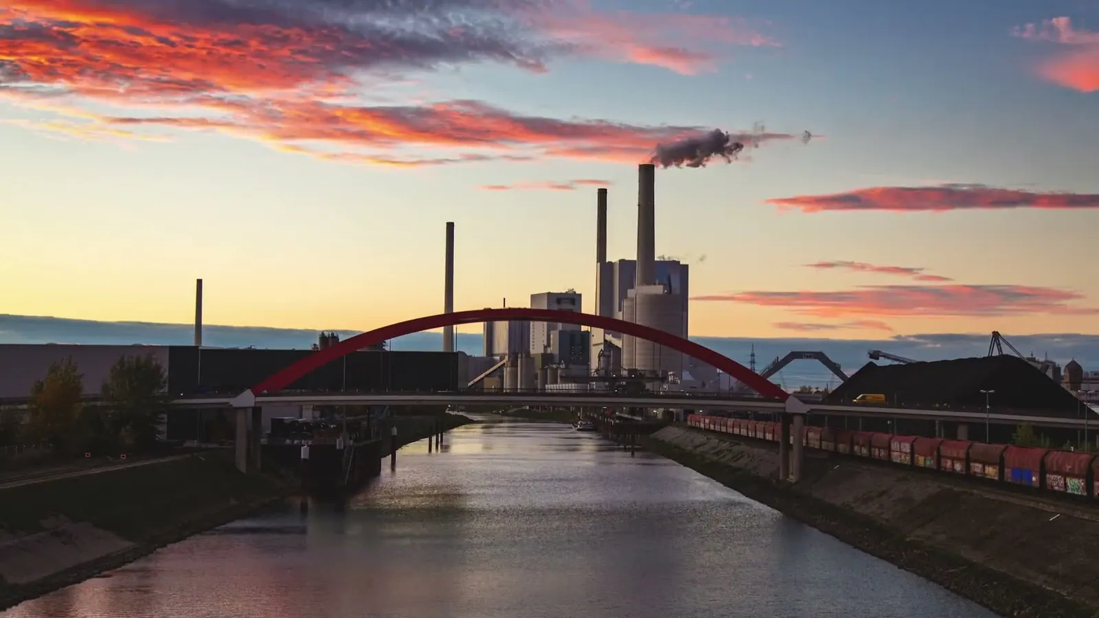 Abendhimmel über einem Kanal mit roter Bogenbrücke und Kraftwerk