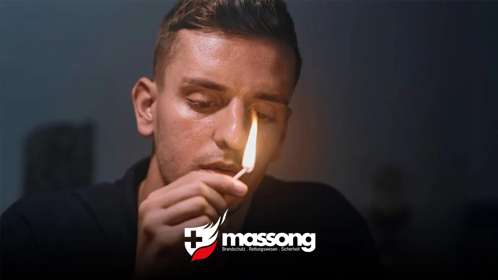 Junger Mann zündet im Dunkeln ein Streichholz an, darunter das Massong-Logo