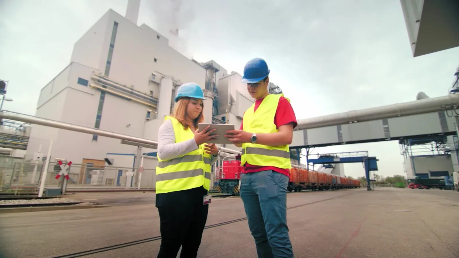 2 Auszubildende in Warnwesten mit Tablet vor einem Kraftwerk