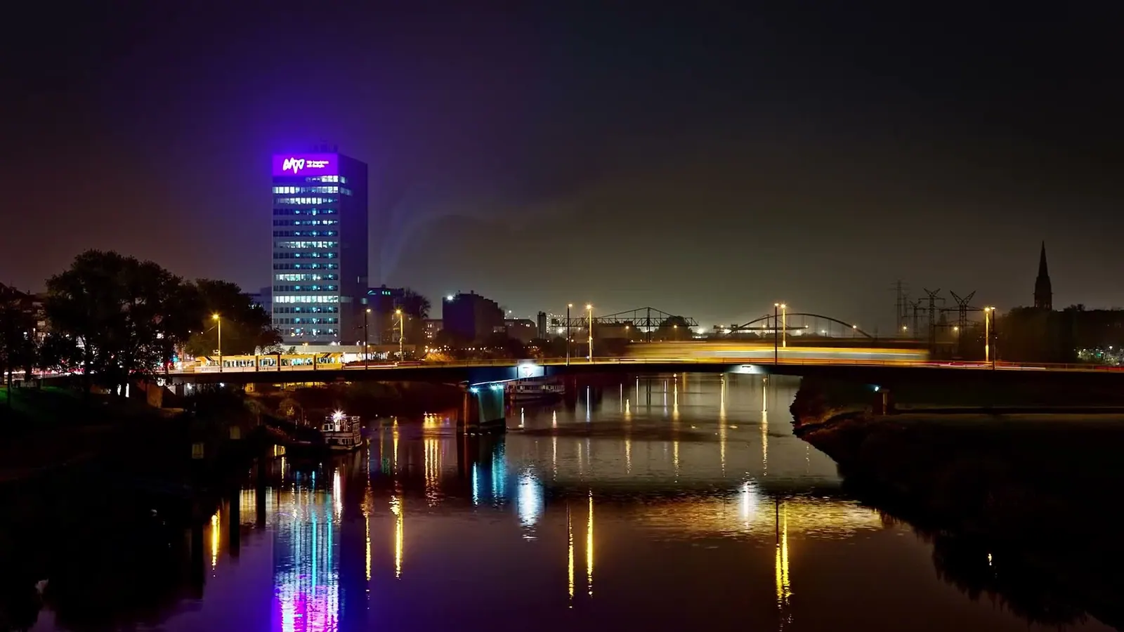 Nächtliche Stadtansicht mit beleuchtetem Hochhaus, das sich im Fluss spiegelt