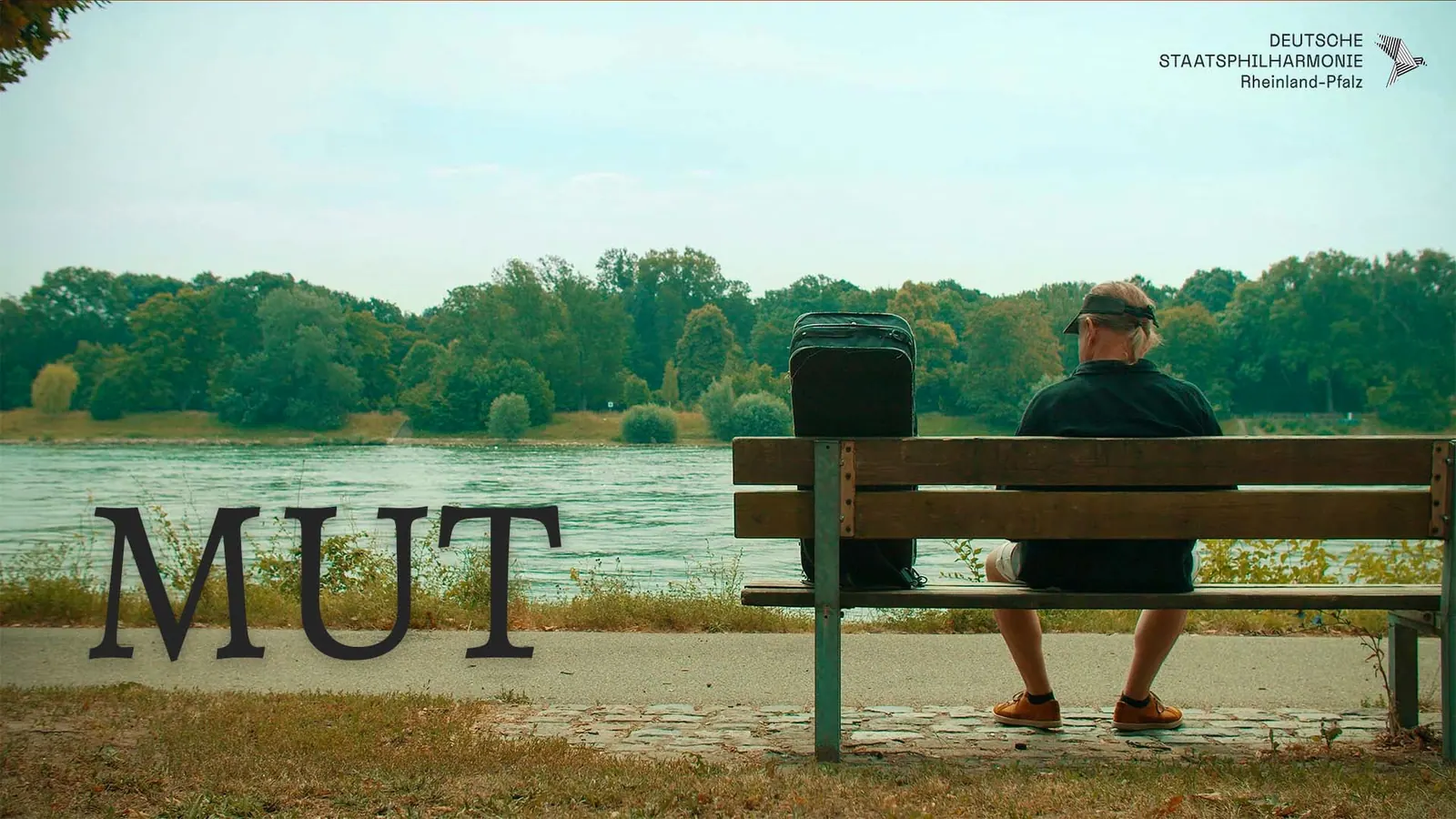 Mann sitzt auf einer Bank am Flussufer, daneben der Titel „Mut“