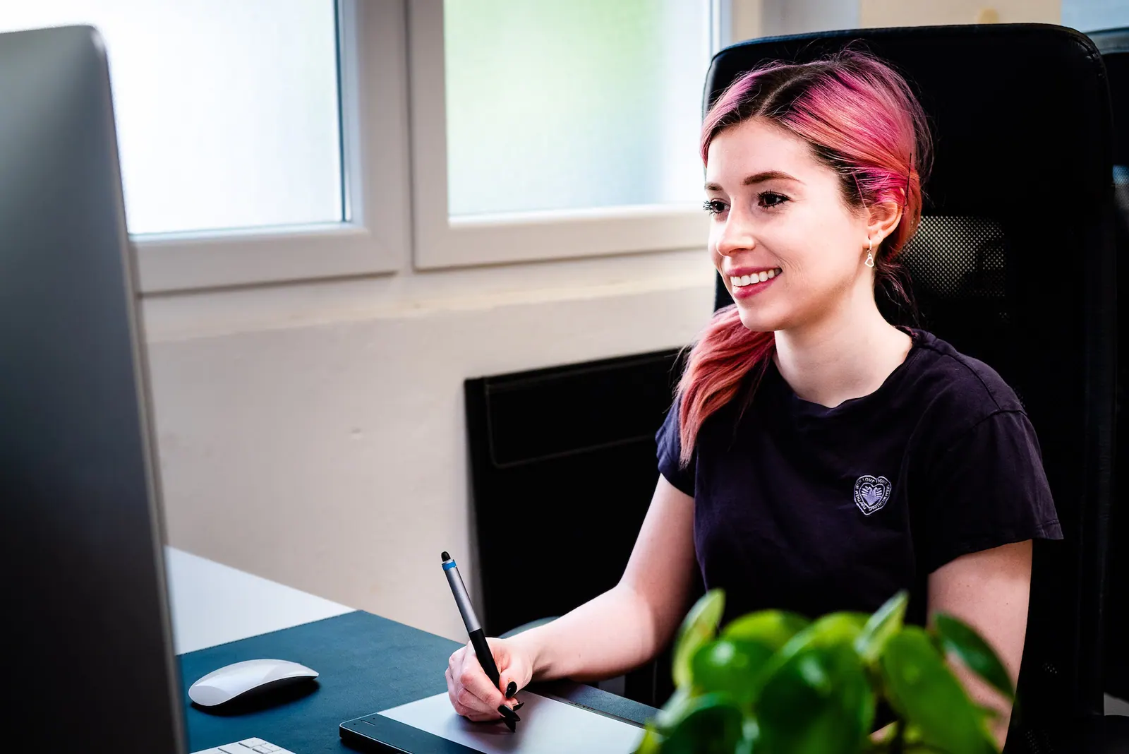 Laura Gehrig aus dem Motion-Design-Team arbeitet lächelnd mit Grafiktablett an ihrem Arbeitsplatz